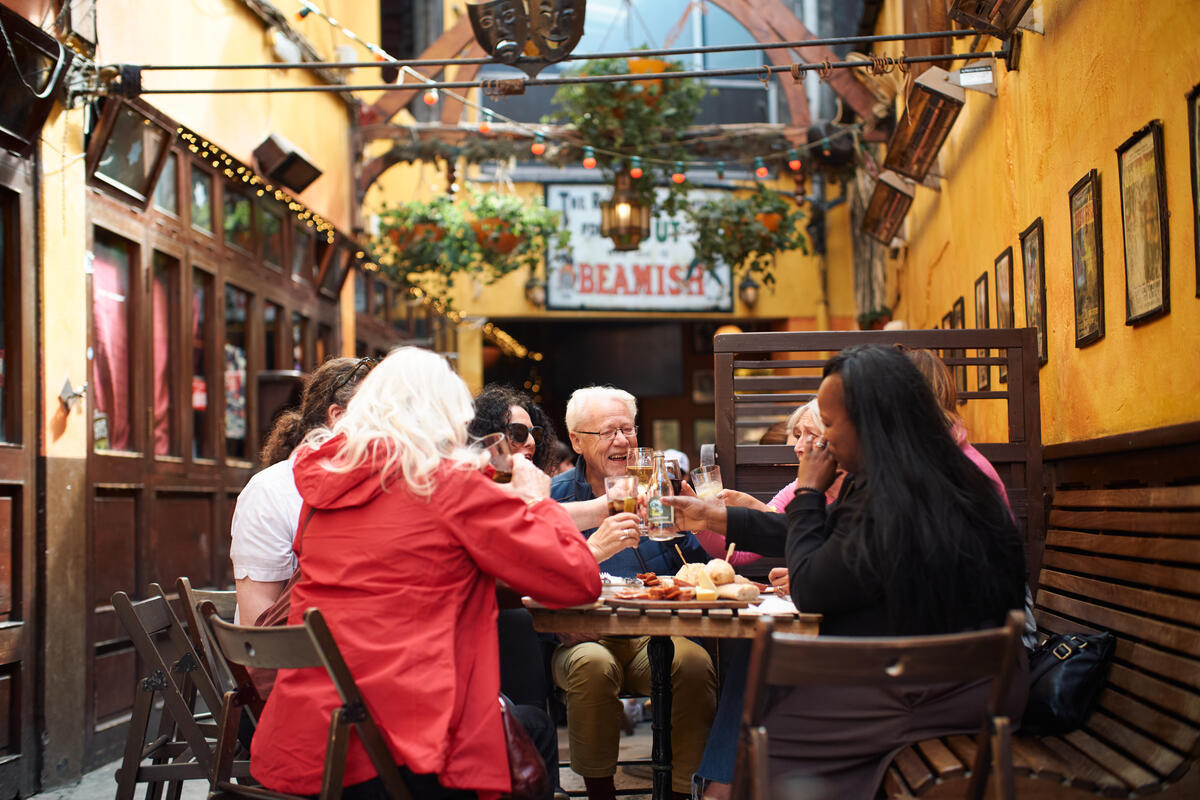 People enjoying drinks in a lively Cork pub courtyard with outdoor seating, warm yellow walls and a relaxed social atmosphere.